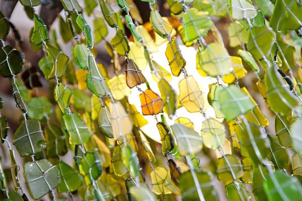 This is a close up of a large glass chandelier, made from recycled materials. The glass beads are green and amber and create a beautiful ambience when backlit. 