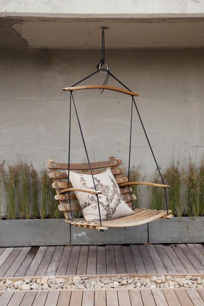 This is a wooden swing chair made from wine barrel staves, hanging over a patio. This hanging chair is accessorised with an eco cushion and is suspended by black yachting rope.