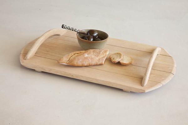 This is a wooden serving tray made from reclaimed oak barrels. It has wooden handles. This serving suggestion contains some olives and a baguette loaf. 