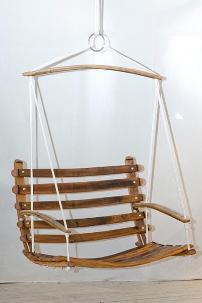 This is a wooden swing chair made from wine barrel staves. This hanging chair is suspended by white yachting rope. 